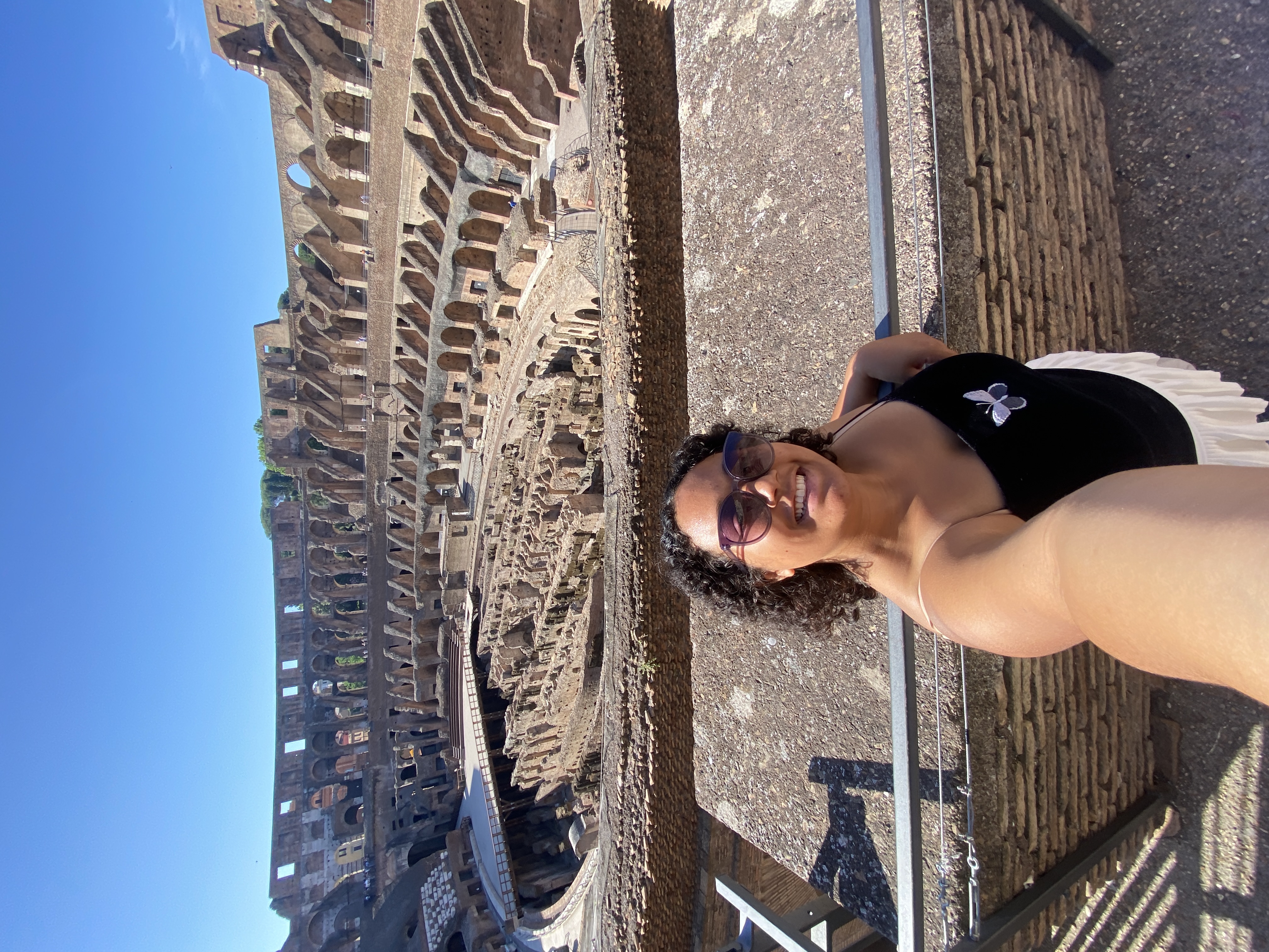 A woman smiling with sunglasses at the Colosseum in Rome