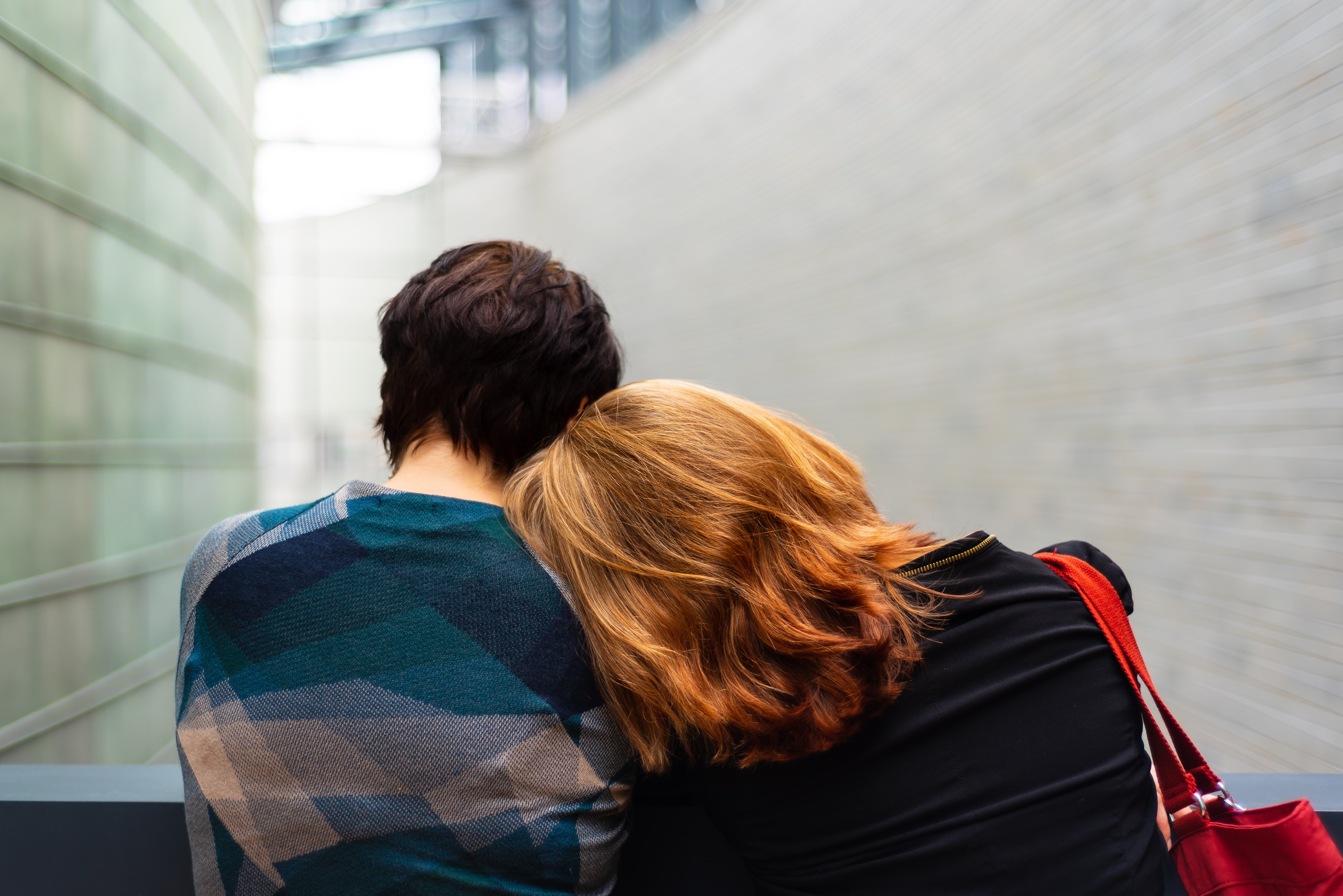 two people resting their heads on each other's shoulders, backs facing the camera