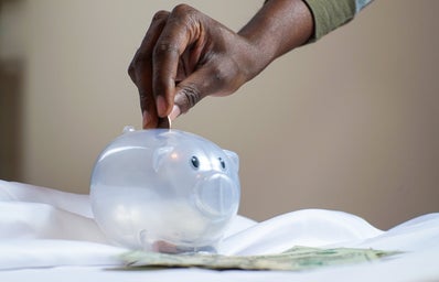 Hand inserting coin into plastic piggy bank