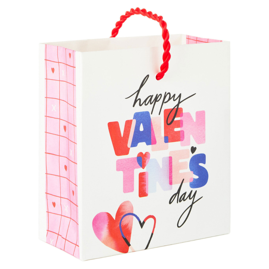 white gift bag with red handle and multi-colored text that reads \