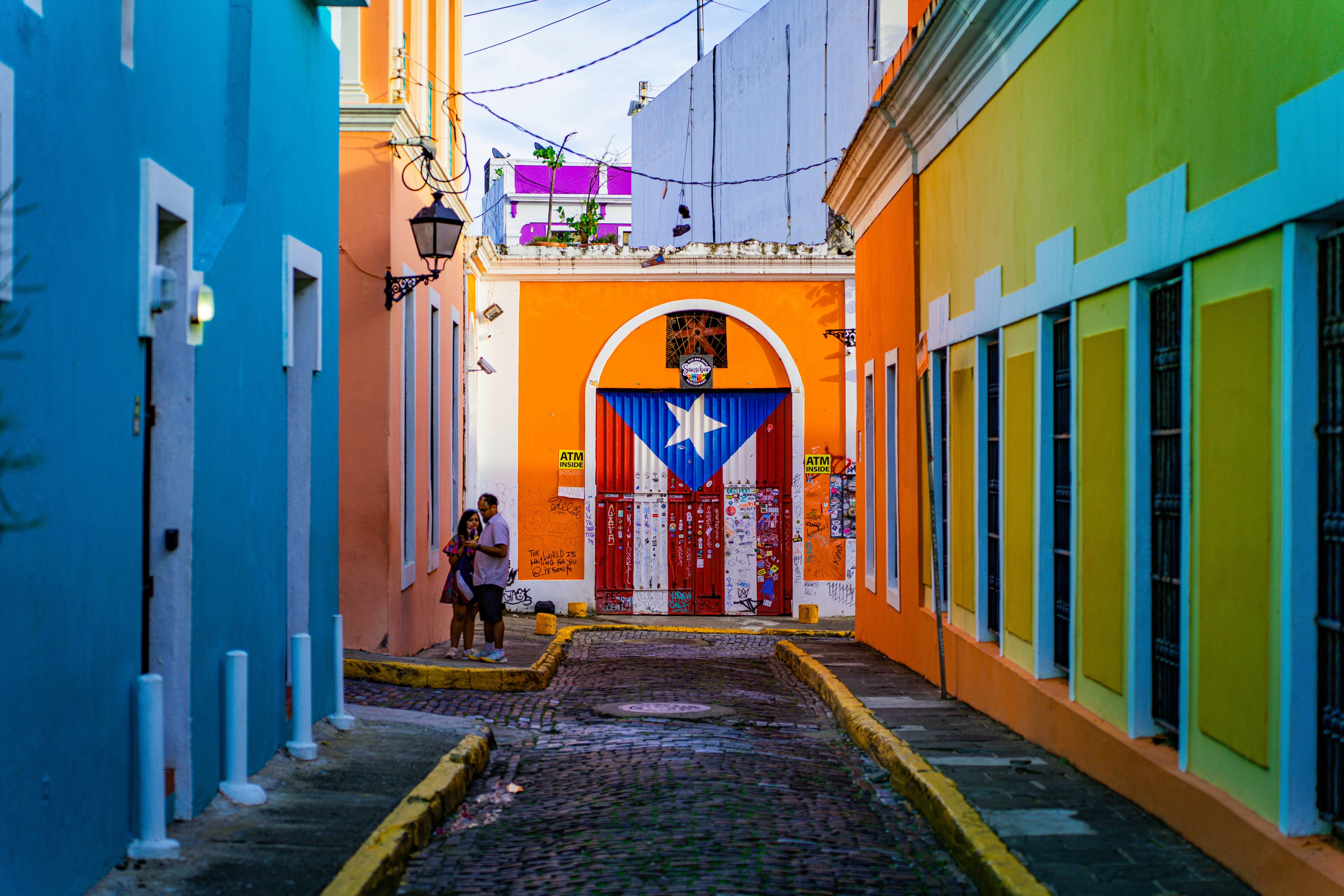 A narrow alleyway in Puerto Rico that is surrounded by colorful buildings, one of which has the Puerto Rican flag painted on it.