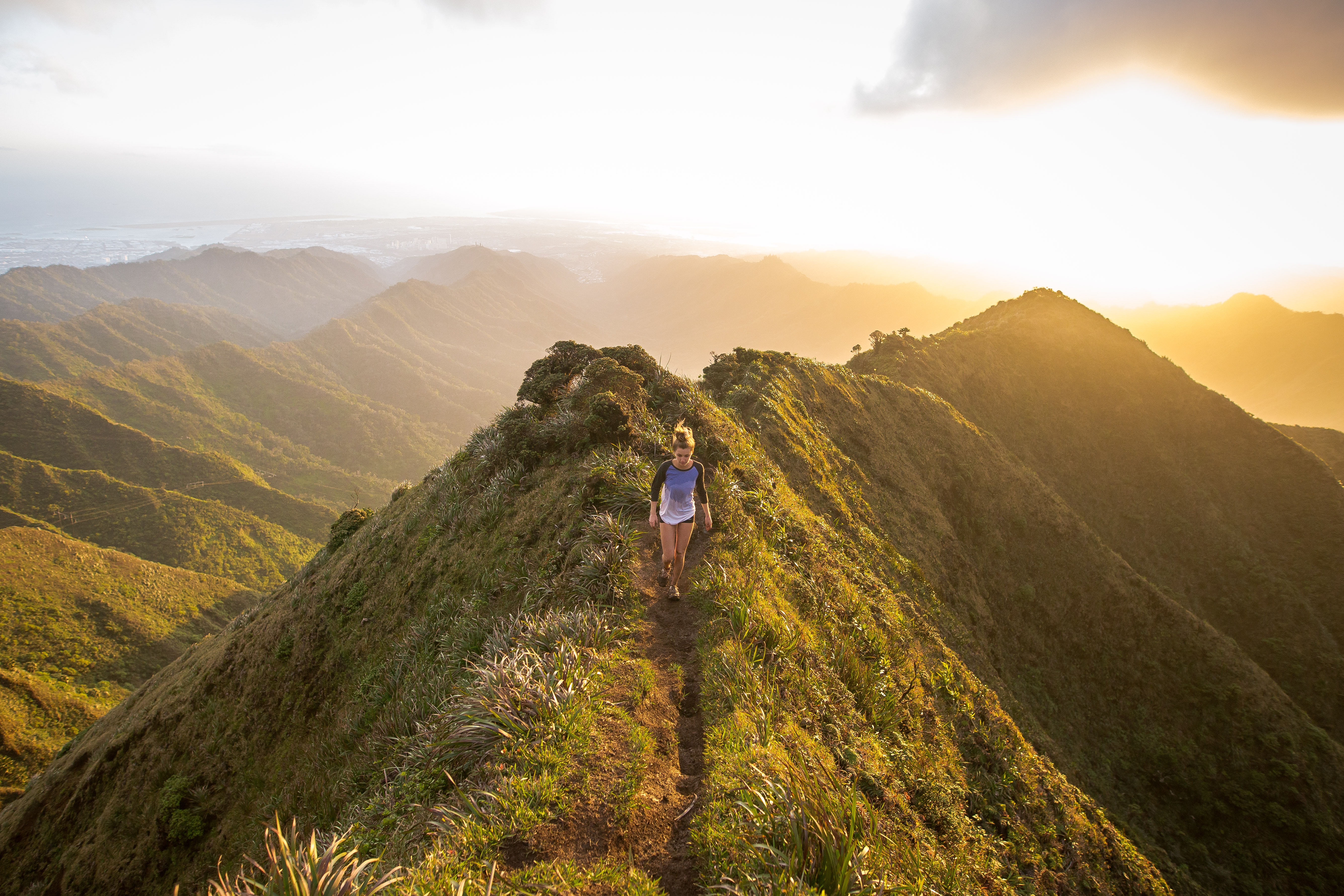 woman walking on a grassy mountain with the sun behind her