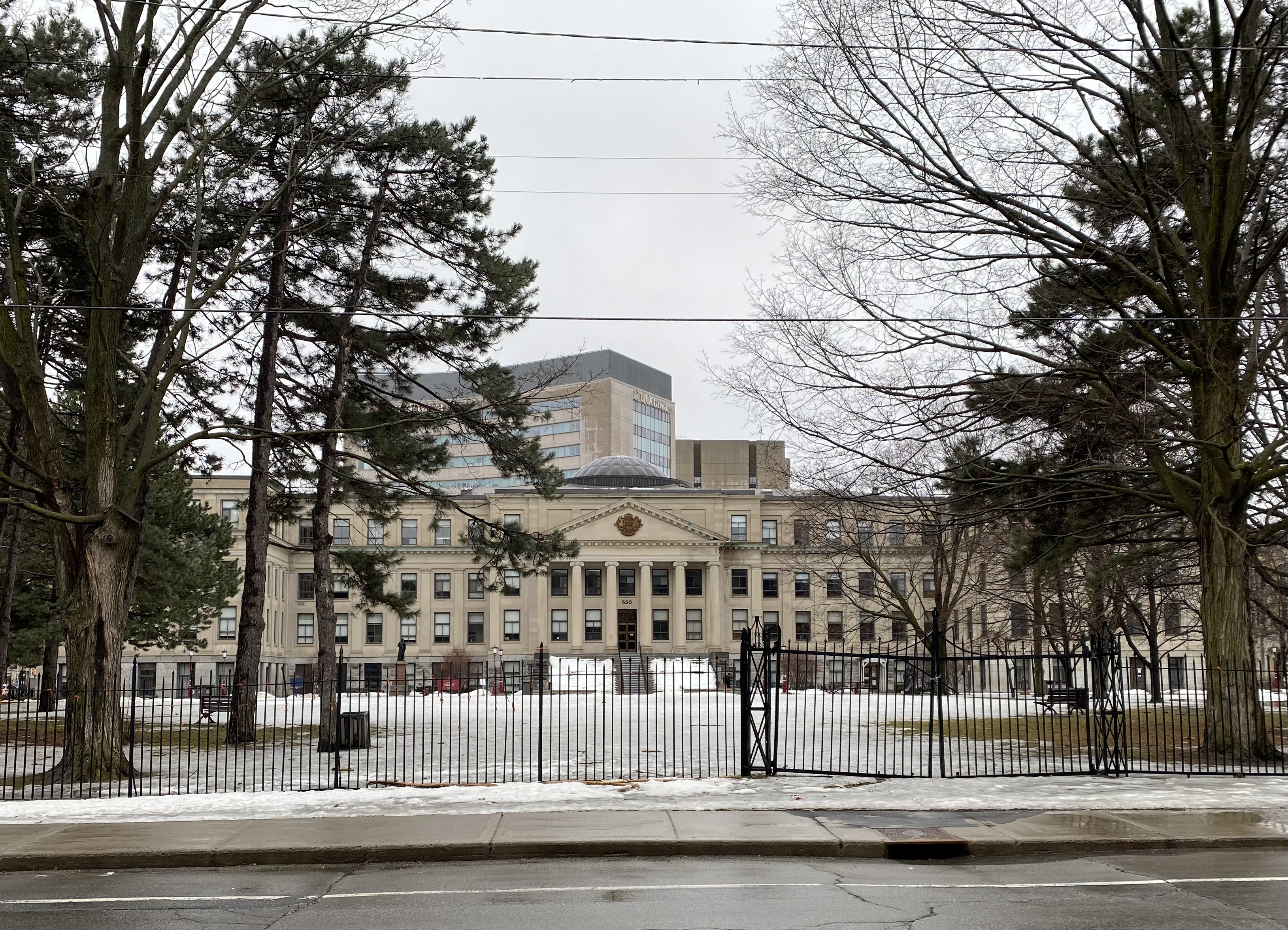 Photo of front of Tabaret Hall in Ottawa, ON taken from across the street through metal fence