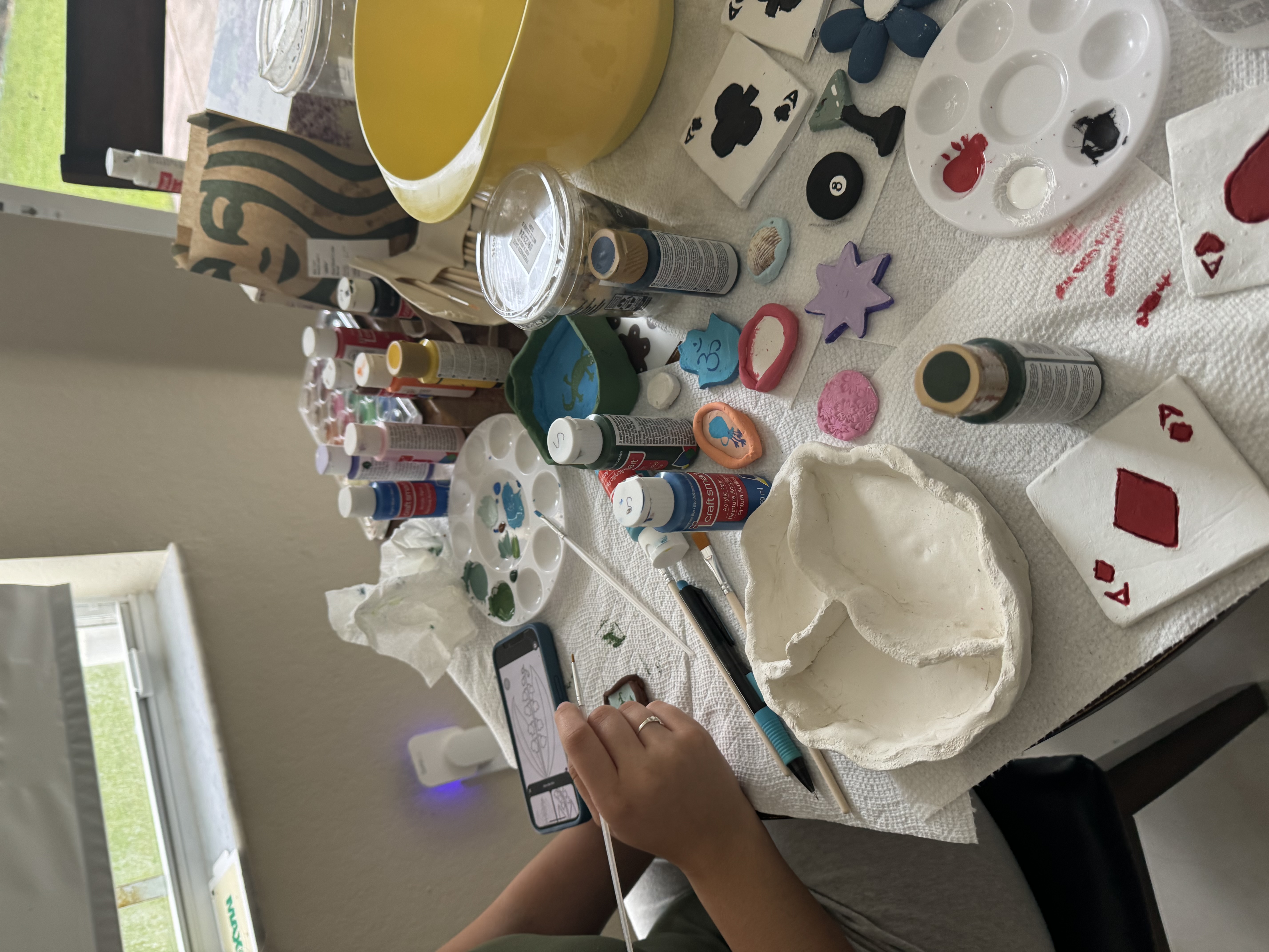Painting and crafting materials spread out on table with girl holding paintbrush