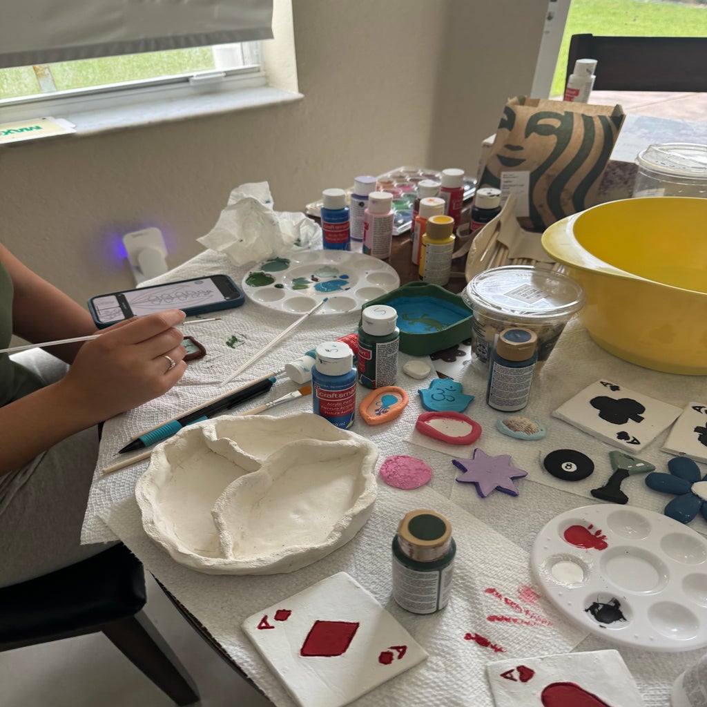 Painting and crafting materials spread out on table with girl holding paintbrush