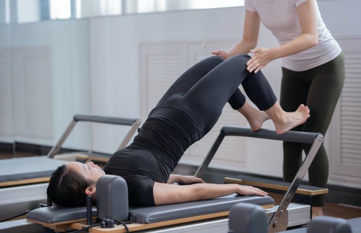An individual on the reformer machine being taught pilates.