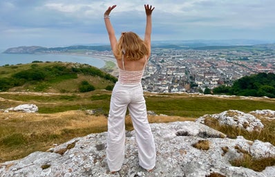 girl standing on cliff with arms up