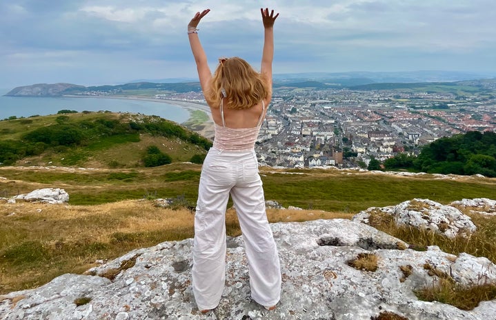 girl standing on cliff with arms up