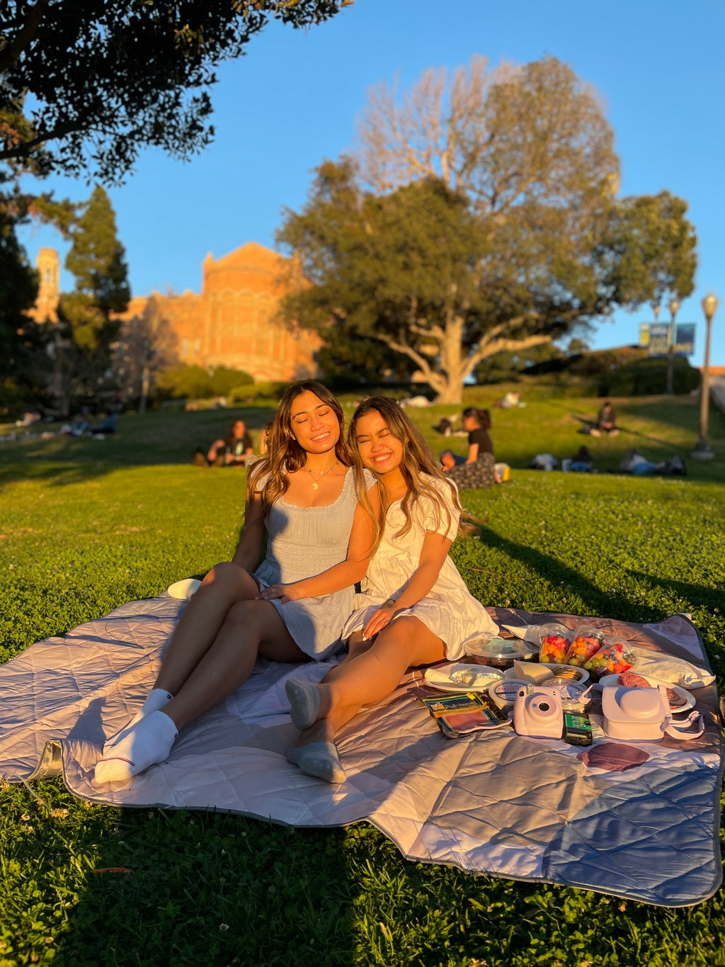 Two girls sit on a picnic blanket outside on UCLA\'s campus.