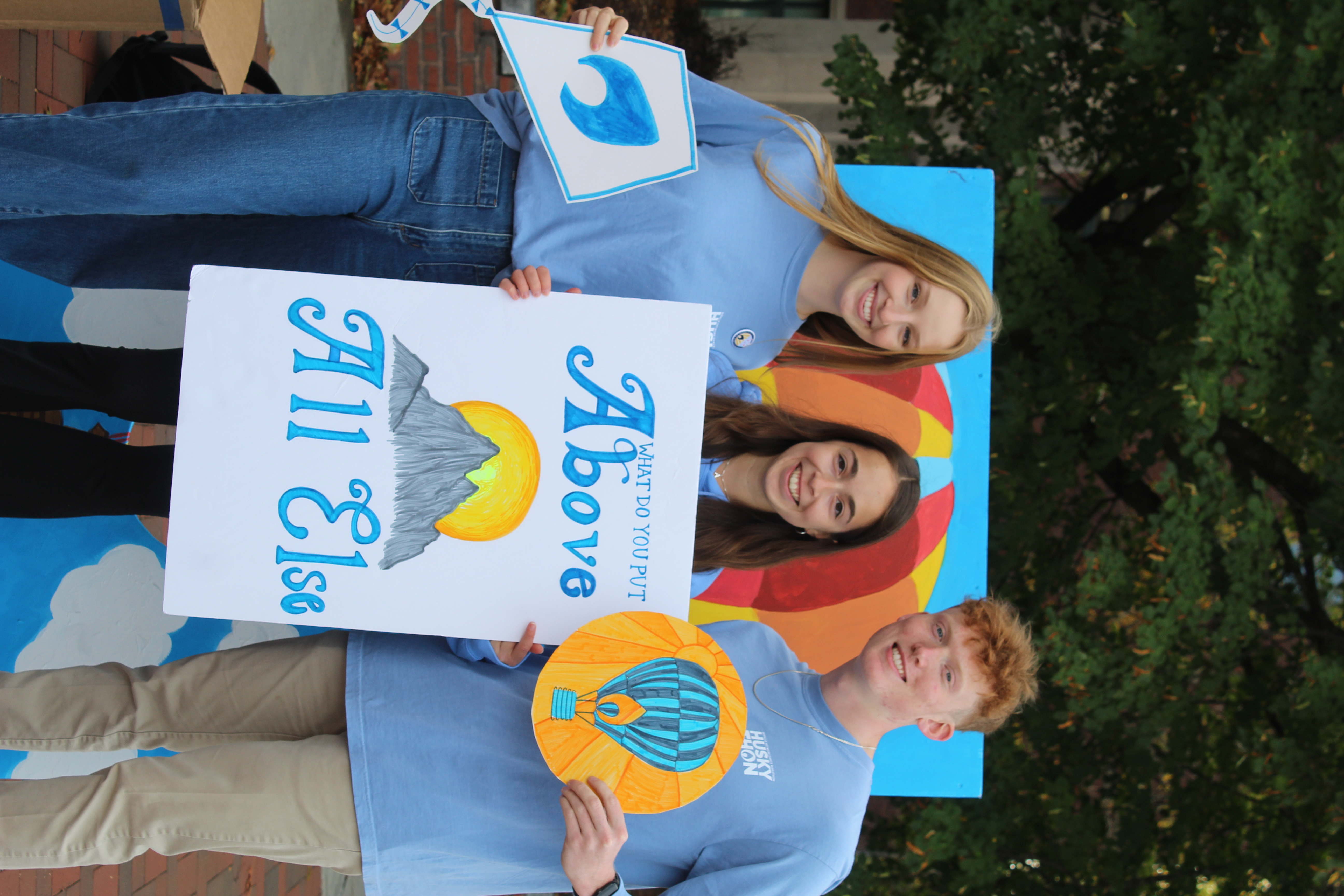 Three people holding HuskyTHON Above All Else signs