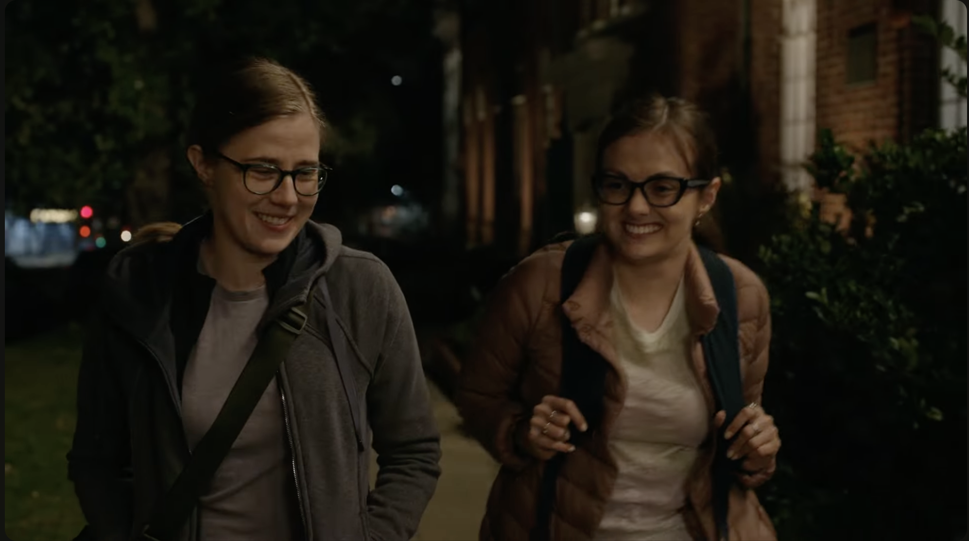Two sisters walking side by side on the sidewalk at night.