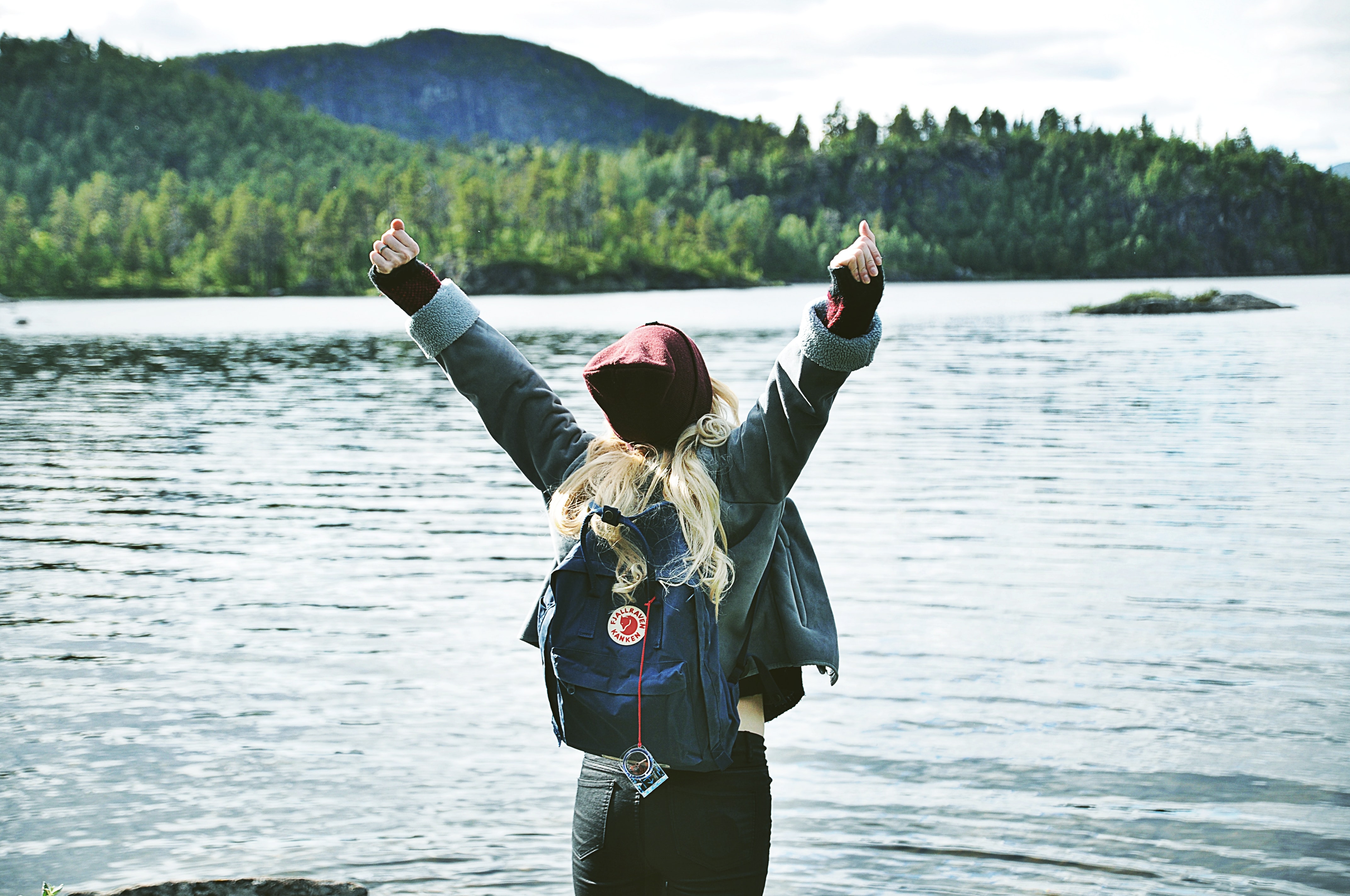 Women with her back facing the camera standing in front of a lake with arms raised