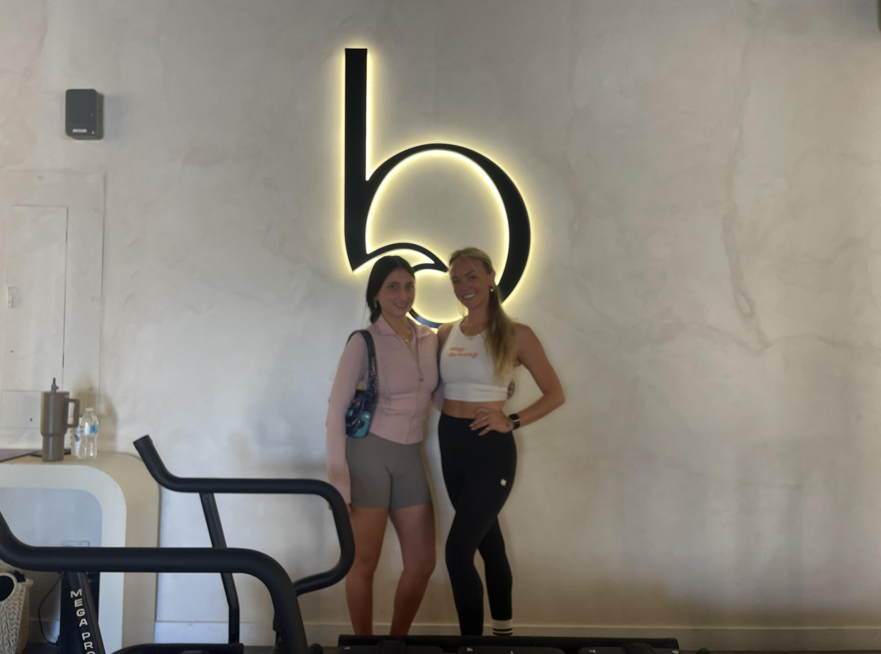 Image of me (Alexa) with my instructor on the right, also named Alexa. We pose in front of the logo from the Lagree studio