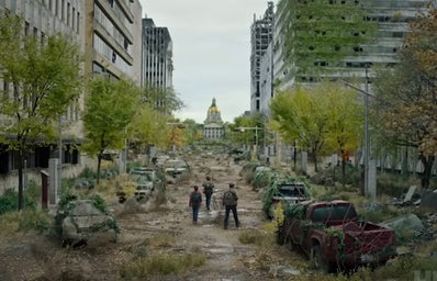 A imagem mostra uma cidade abandonada com três pessoas andando pela rua.