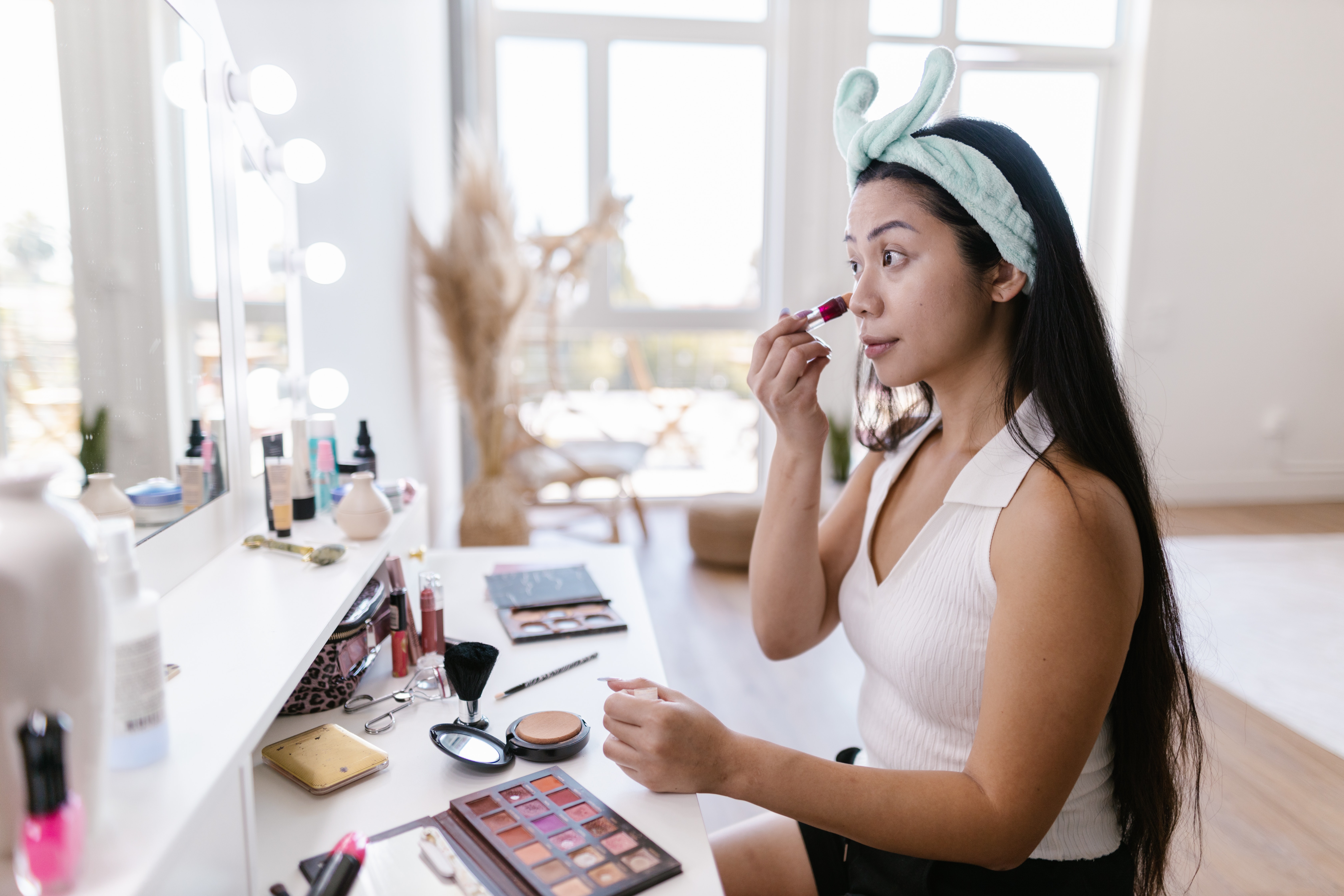 A woman sitting in front of a vanity doing her makeup