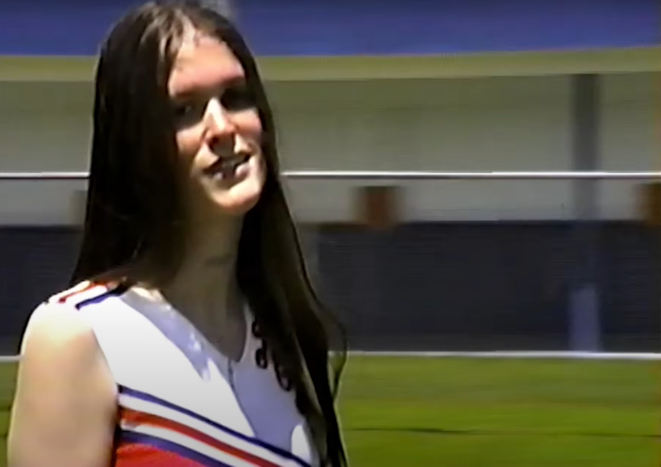 Ethel Cain (young white woman) smiling at camera. She is wearing a red cheerleader uniform.