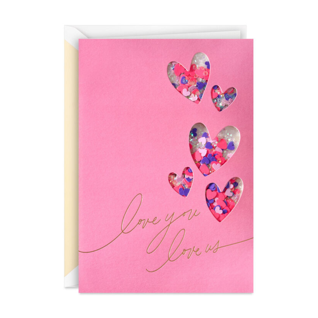 Pink greeting card with heart-shaped cutouts containing colorful confetti. Gold cursive text reads \