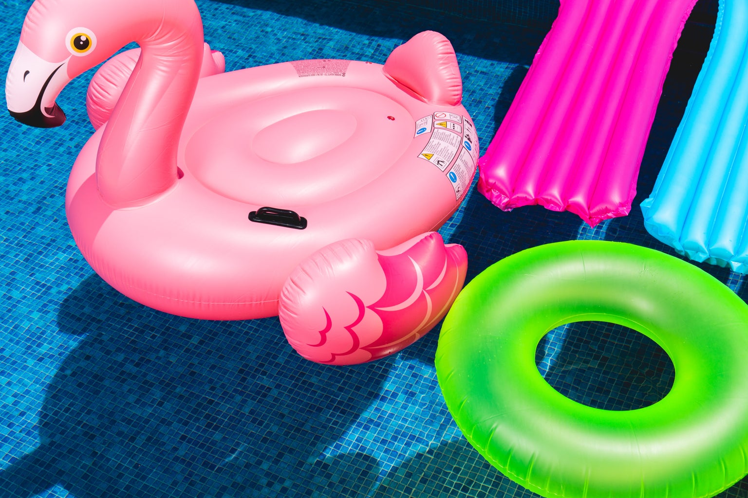 Pink inflatable flamingo in pool next to neon green inflatable.