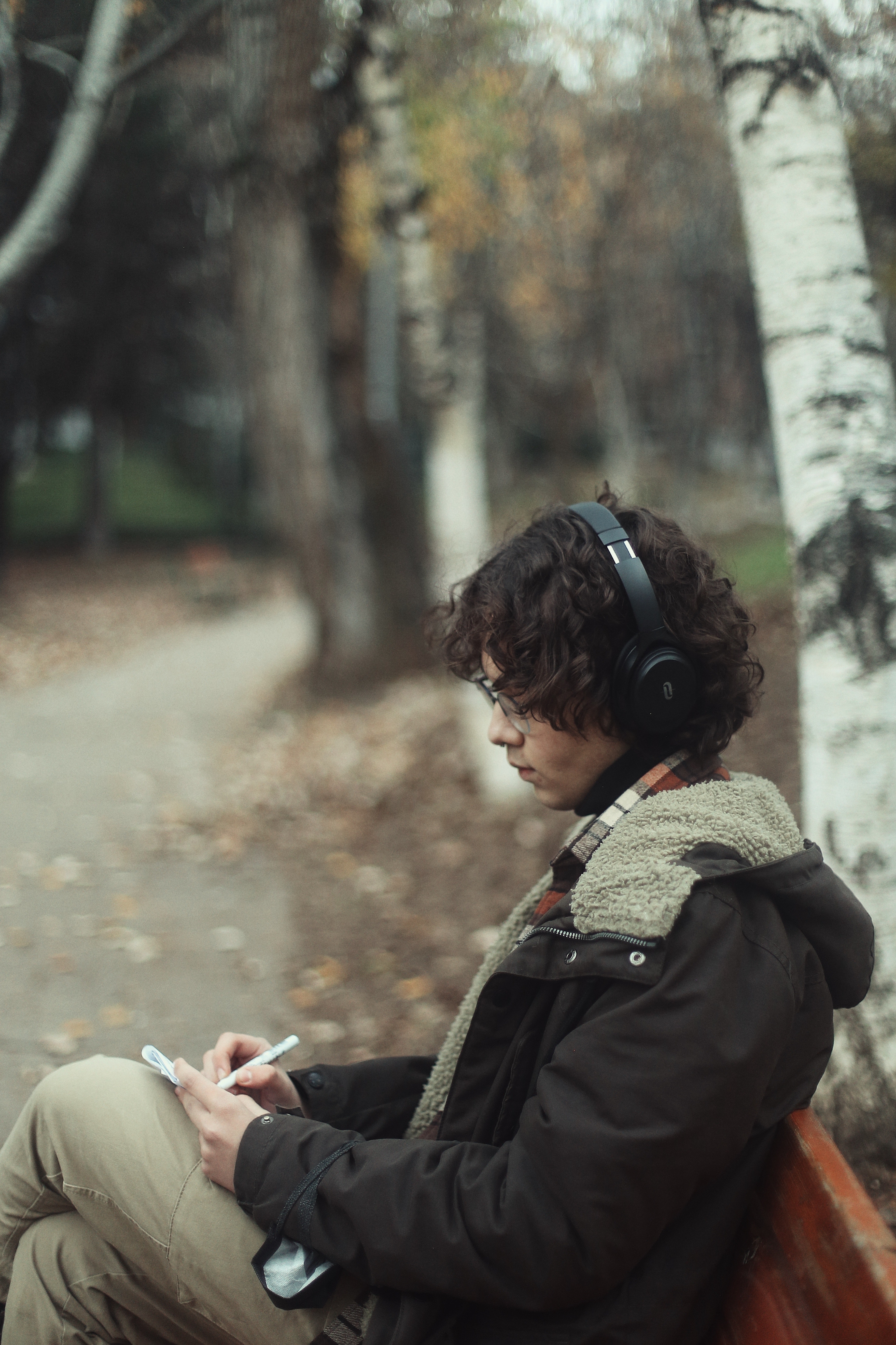 Person wearing headphones sitting on a bench with a fall background