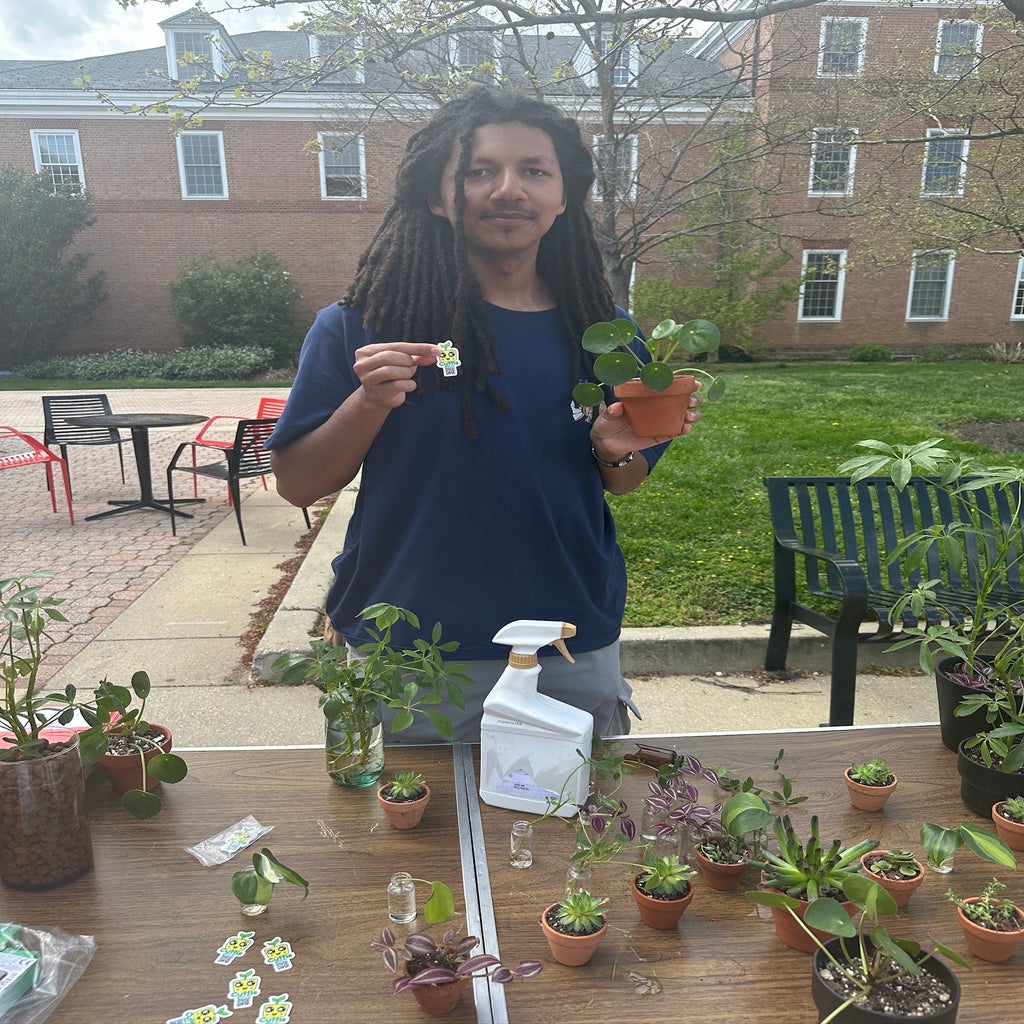 A photo of Ethan Bikos at his Cuttis Plants table posing with his products and his free sticker with a QR code to his website.