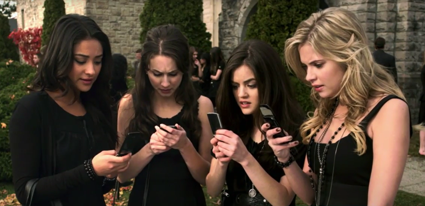 Four girls standing, reading a text from their phones.