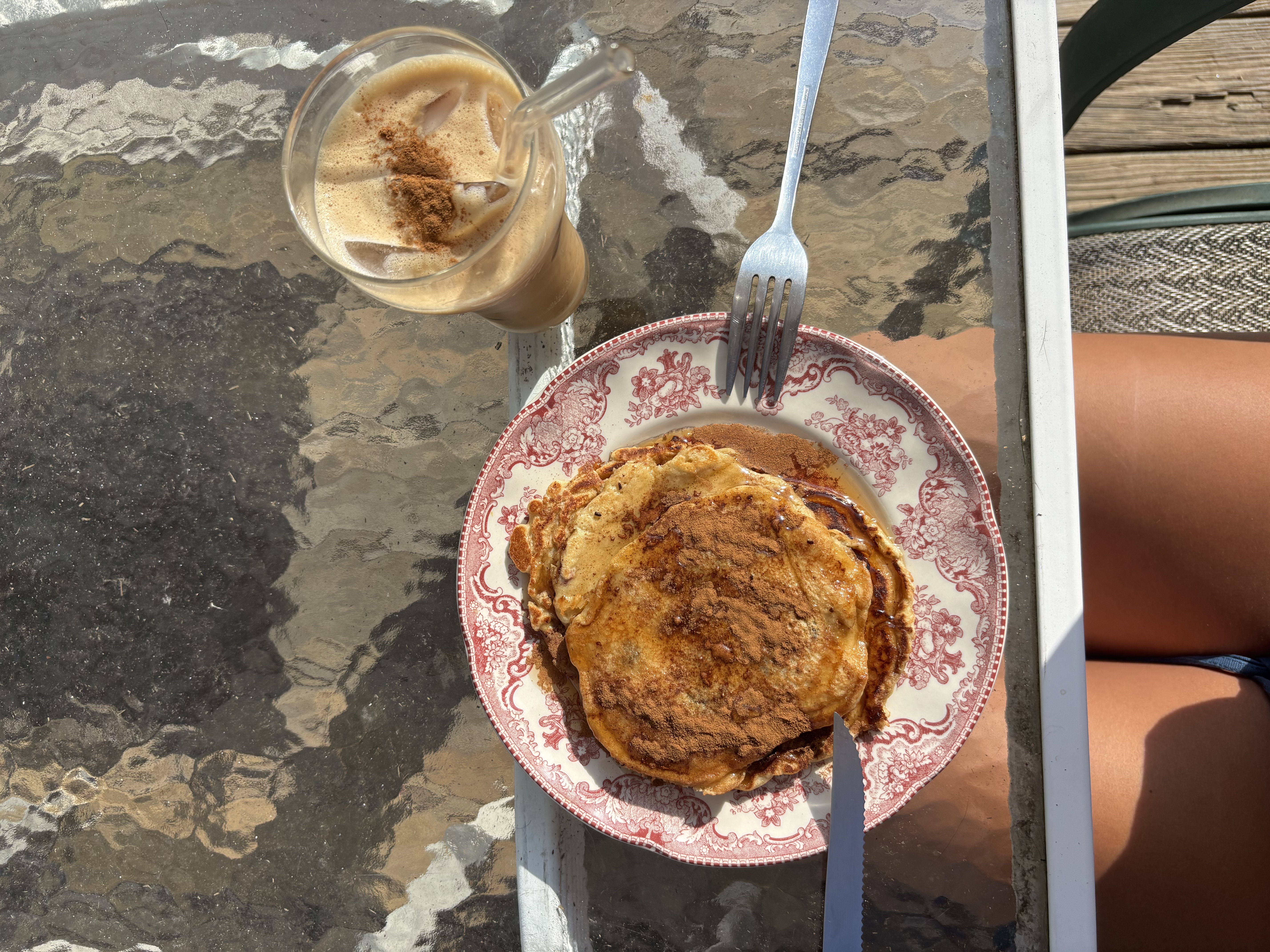 Picture of a plate full of pancakes on a glass table next to a coffee cup.