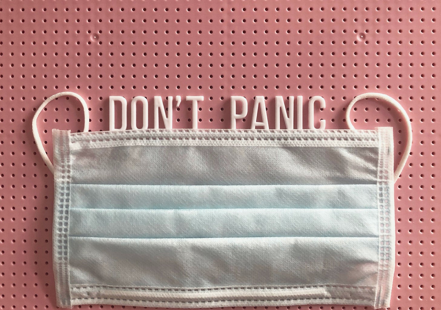 reuseable surgical mask with phrase \"don\'t panic\" on a pink letter board
