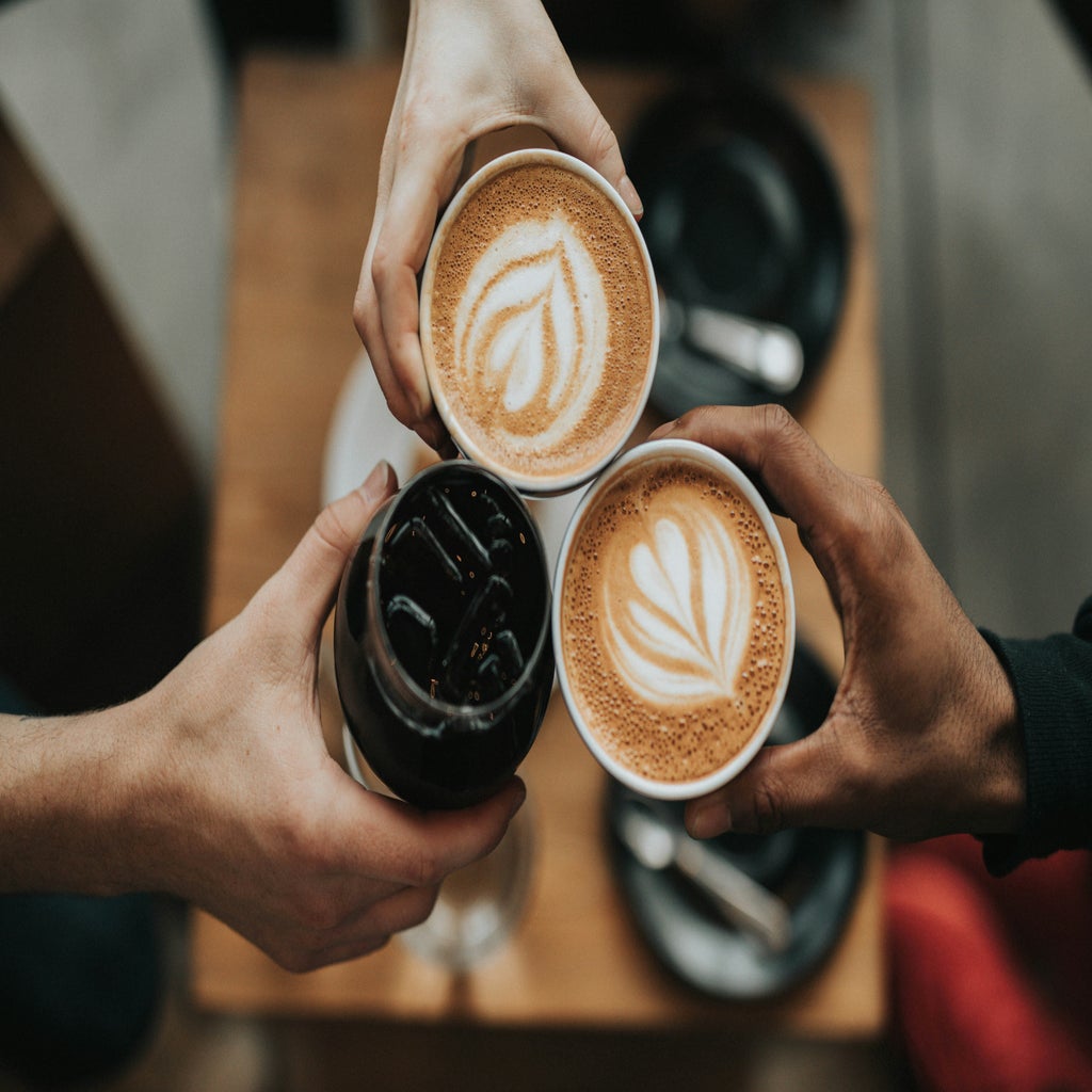 Three hands holding lattes and iced coffee