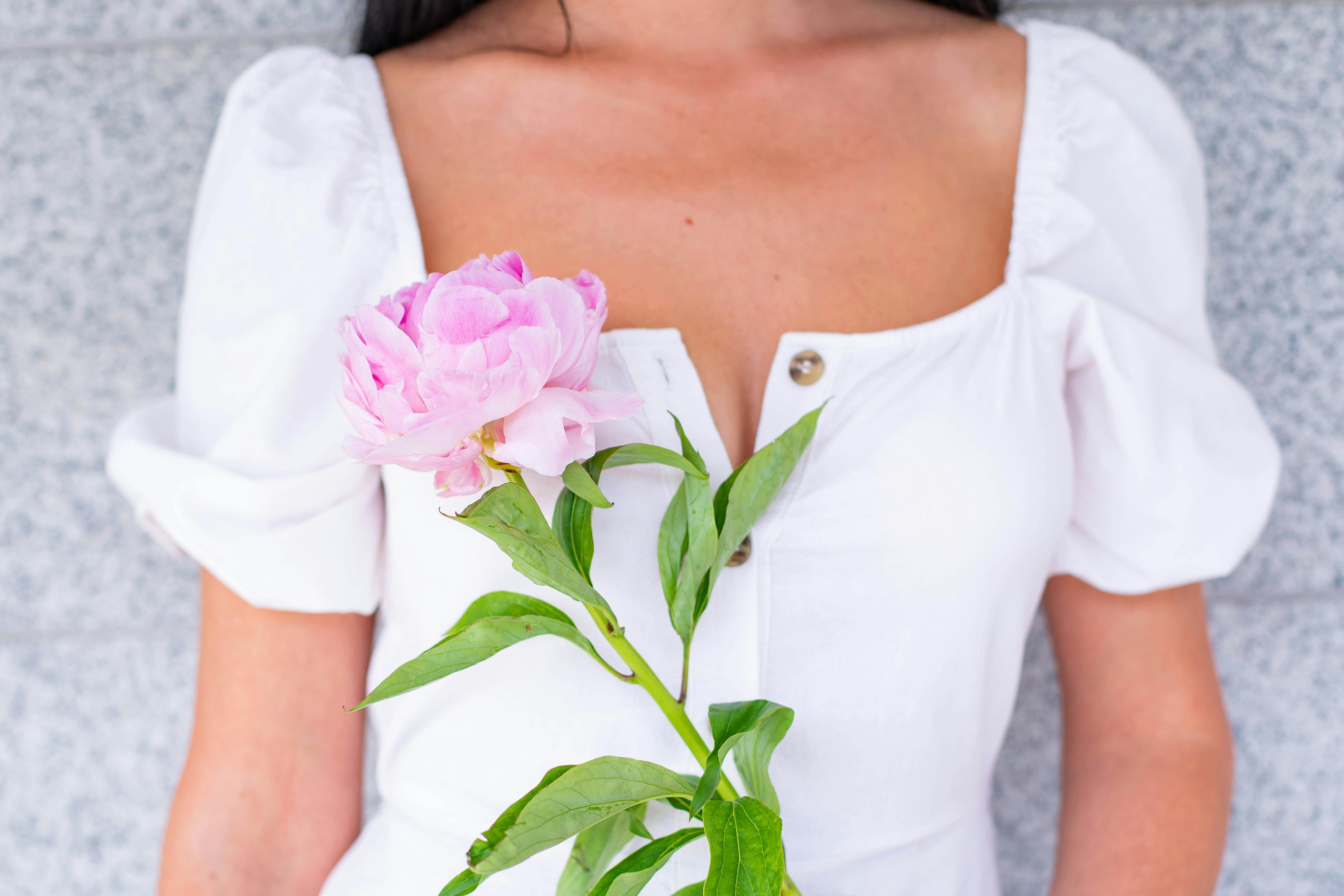 woman in a white dress holding a pink flower