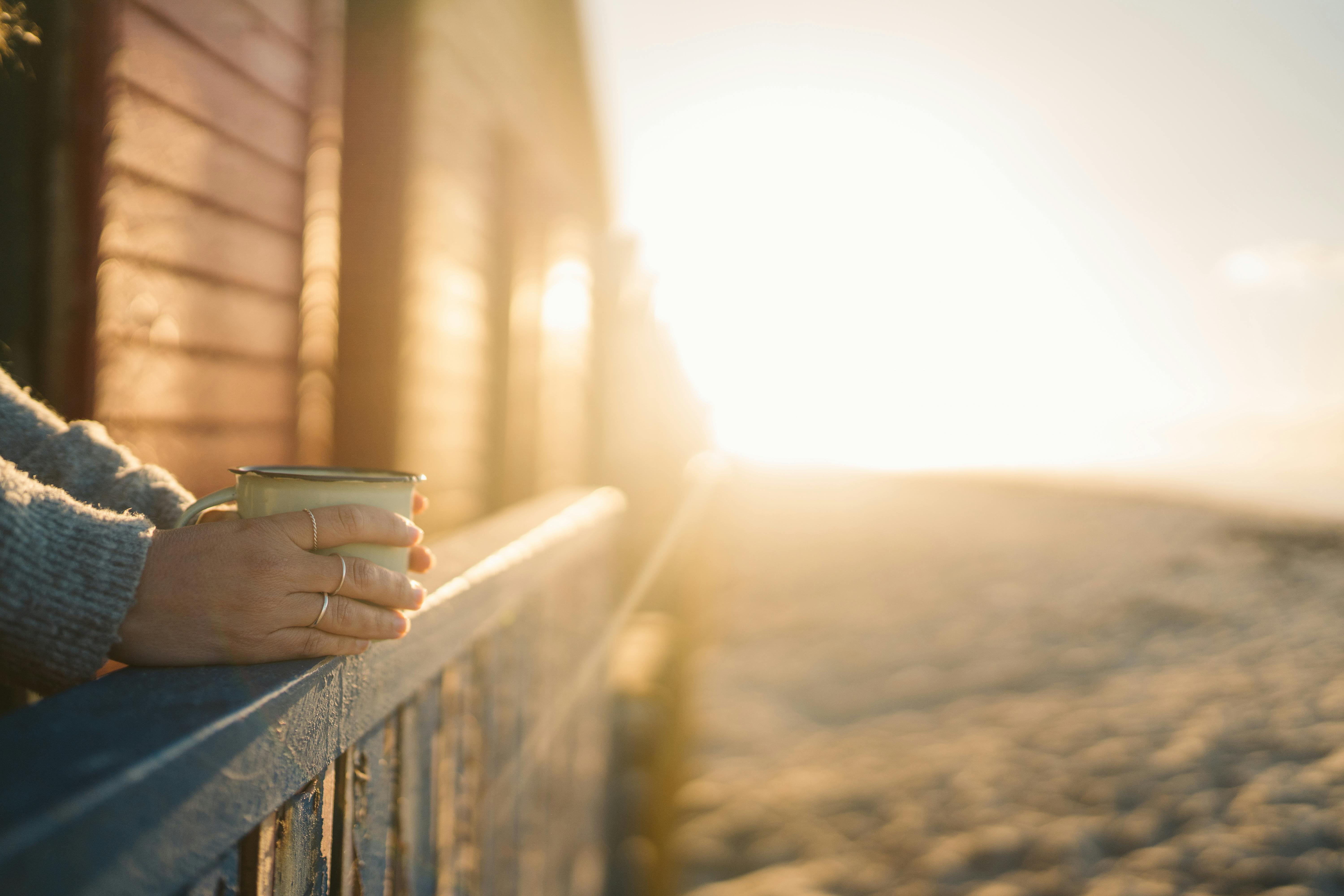 A woman holding a cup of coffee looking out at the beach.