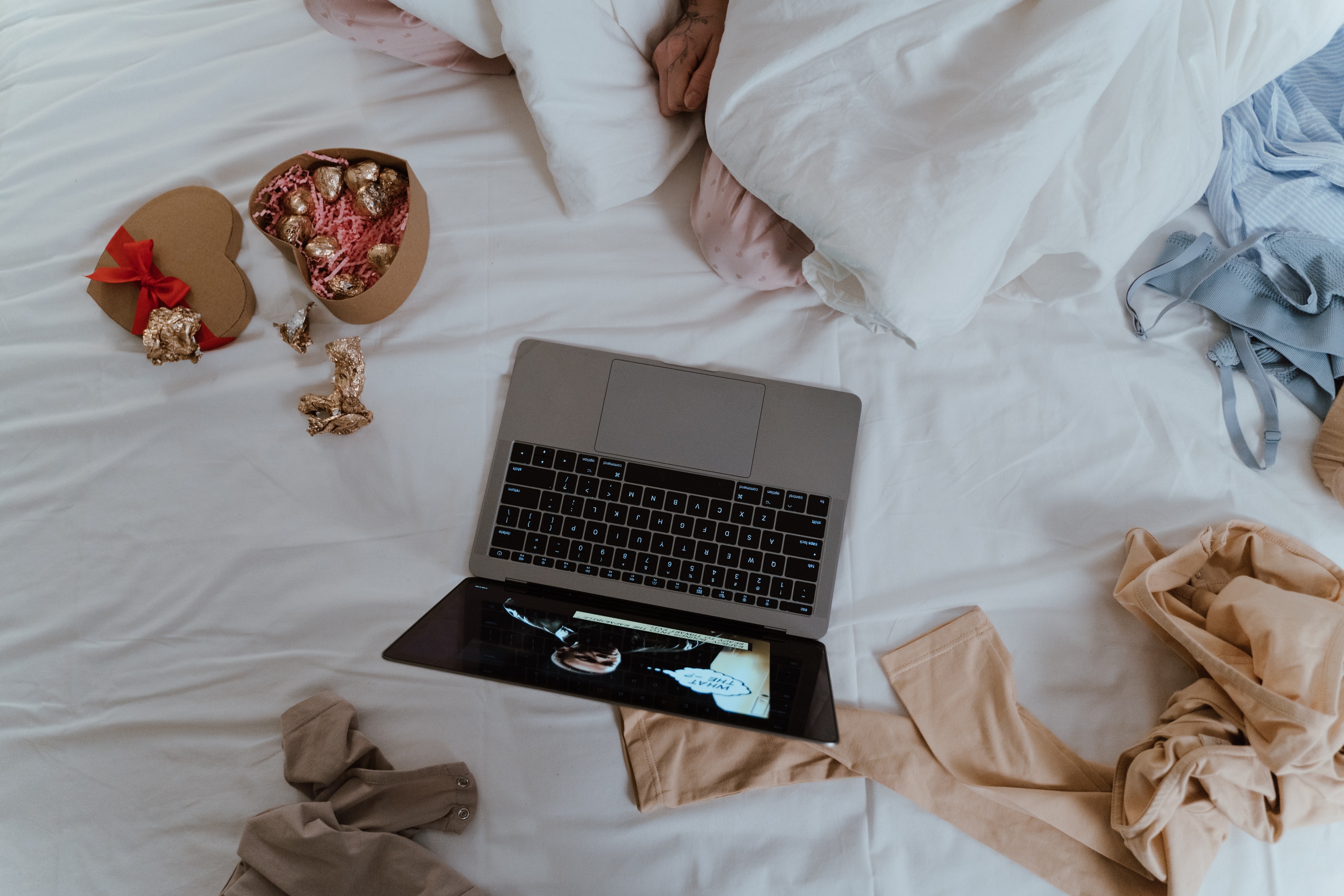 A messy bed with someone watching a show on a laptop and eating valentines chocolates alone