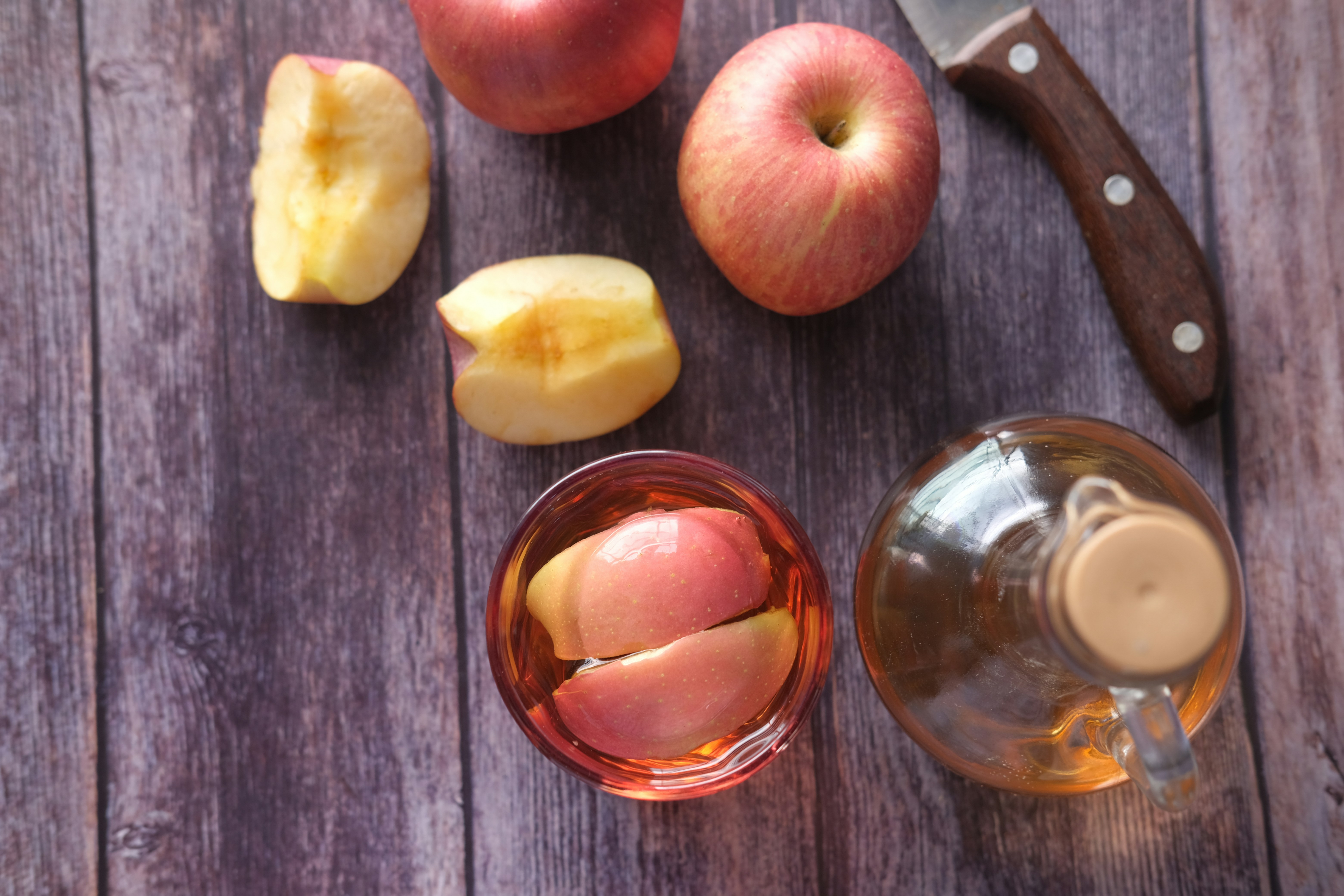 Apples sliced on a table next to a bottle of juice or vinegar