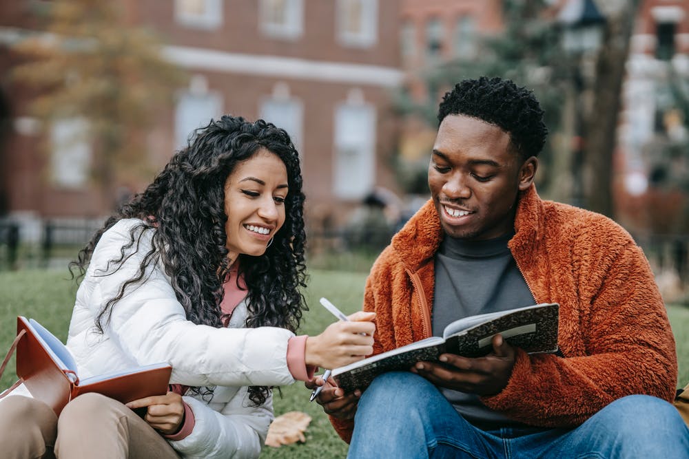 Two students sitting in the grass talking and studying LLC article