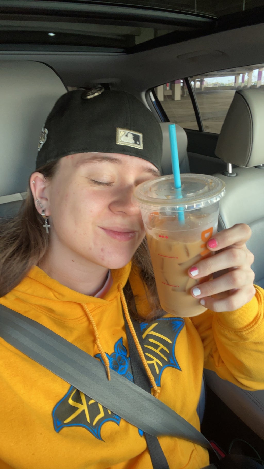 A selfie of Mackenzie Szabo holding a Dunkin Donuts drink in her car