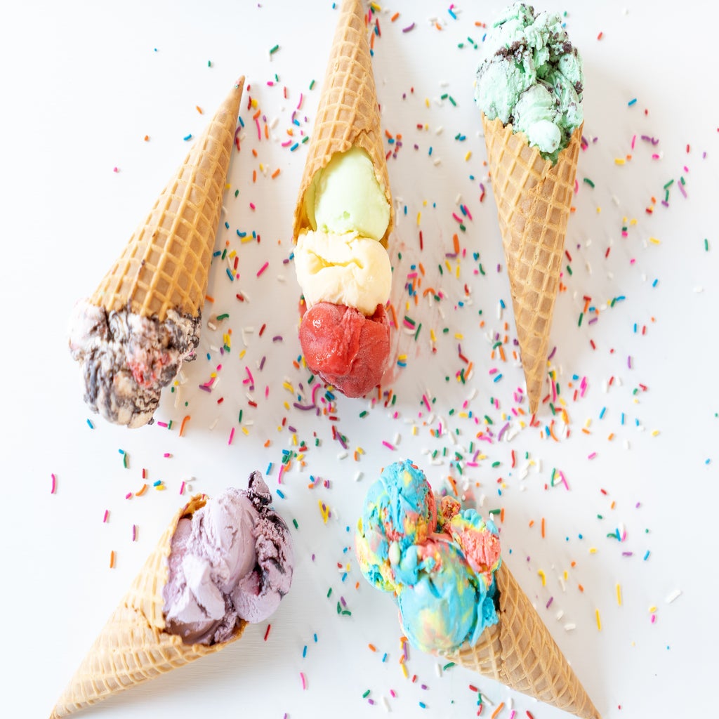 Five ice cream cones of various colors with sprinkles all scattered on a white countertop